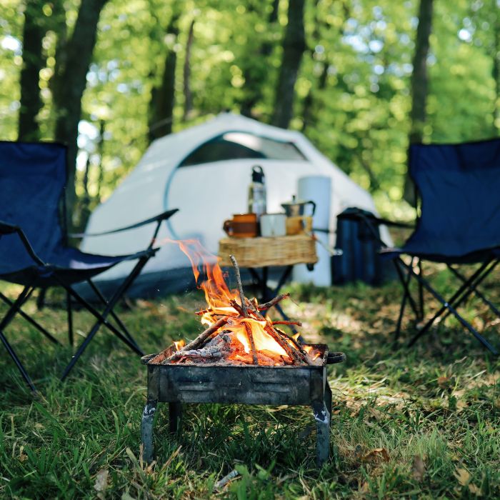 camp fire with tent, chairs, and serene setting